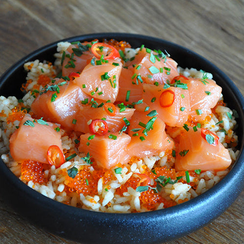 Bowl of salmon and rice dish with garnishes on a wooden table