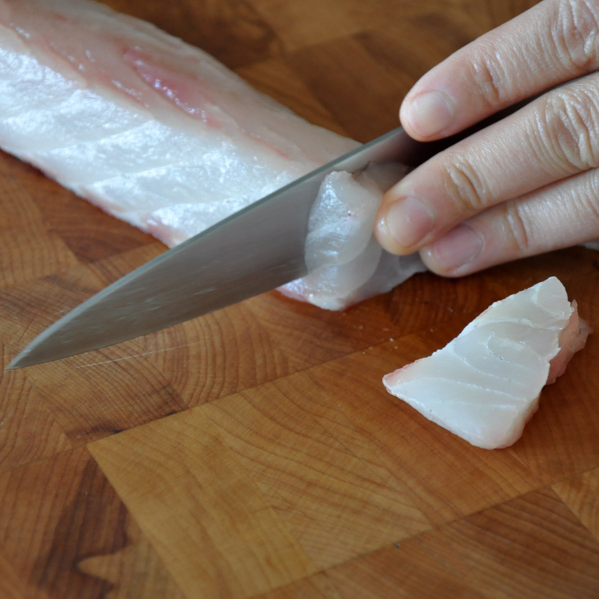 Person cutting sashimi on a wooden cutting board with a knife.