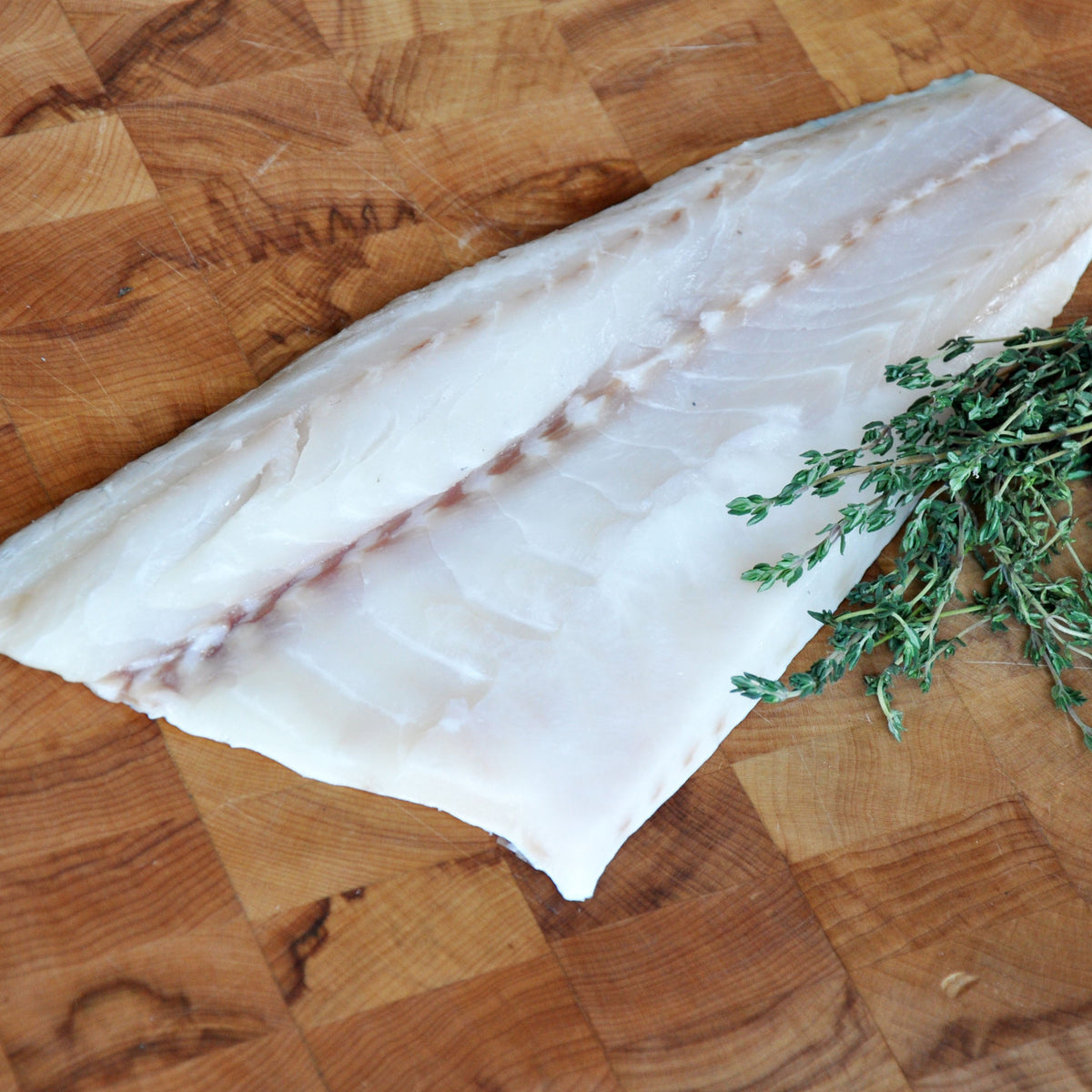 Raw fish fillet on a wooden cutting board with herbs