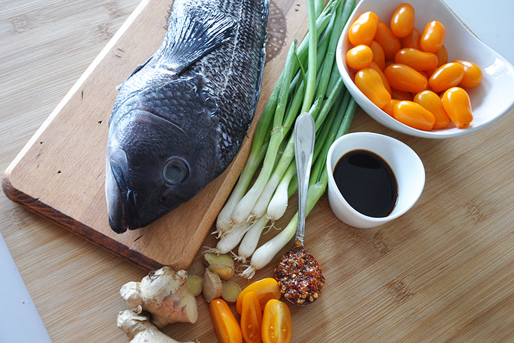 whole fish on a cutting board with vegetables and sauces on a wooden surface