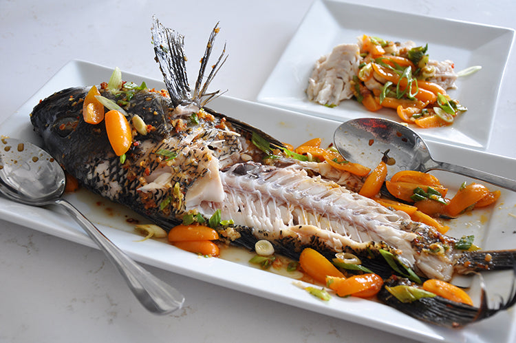 whole black sea bass cooked and half eaten with tomatoes and herbs